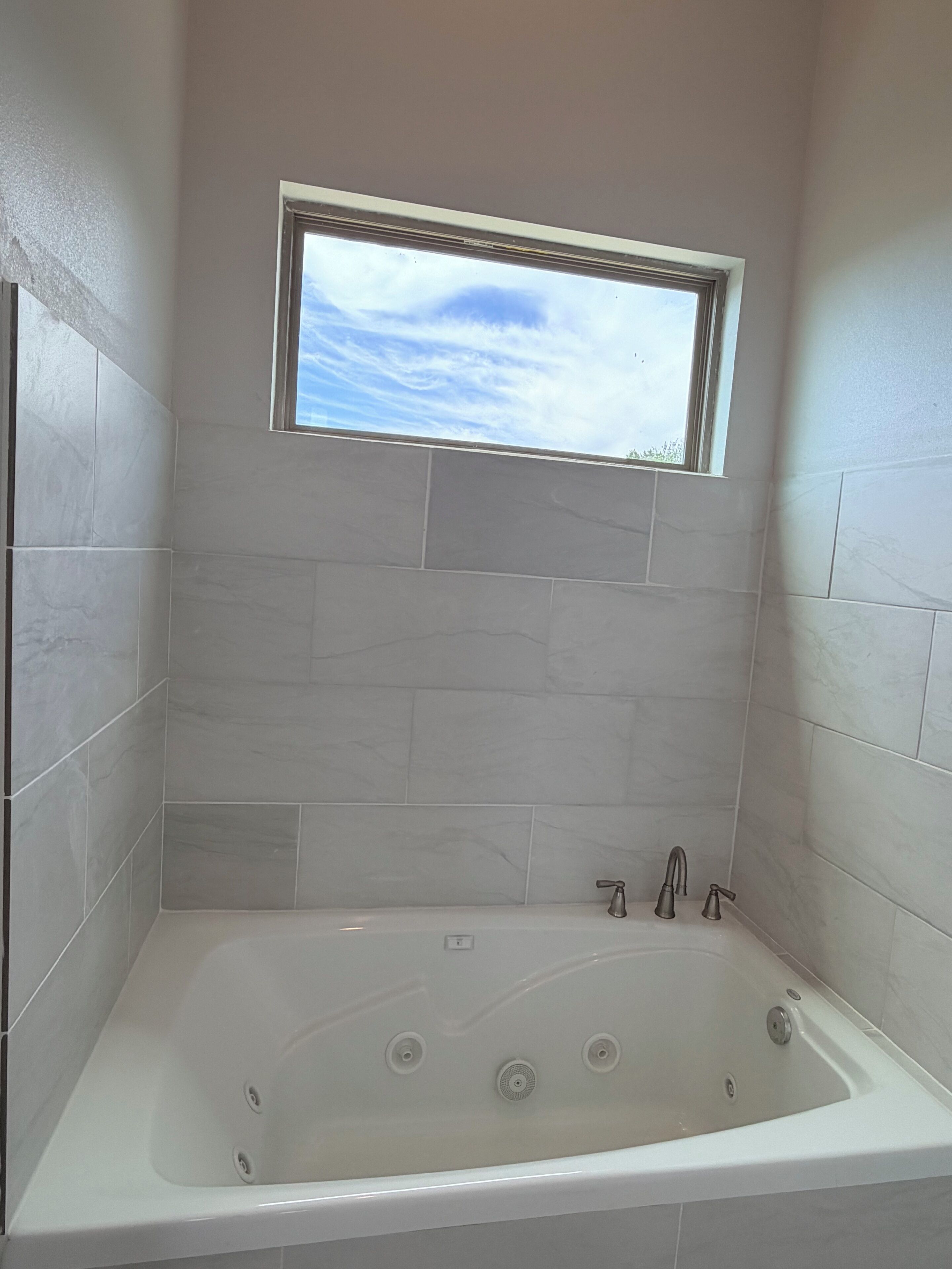 A bathroom with a bathtub, a window, and tiled walls.
