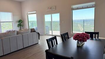 A spacious living area with a sofa, dining table, chairs, and large windows offering a view of the outdoors.