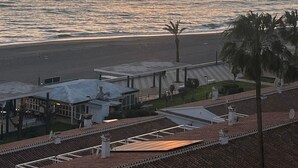 Sonnenuntergang an der Küste mit Strand, Palmen und einem Gebäude mit Ziegeldach.