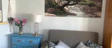 A living room with a sofa, a coffee table, a blue cabinet, a wall-mounted lamp, and a painting of a landscape.