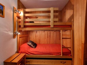 A bunk bed with a red mattress and a pillow, a wooden desk, and a wall-mounted light fixture. - 100m from ski slopes, 6th floor, view mountain, balcony, tv, 25m², Les Orres (Les Orres)