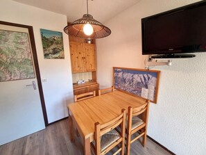 A wooden dining table with chairs, a hanging light fixture, a mounted flat-screen TV, and a framed map on the wall. - 100m from ski slopes, 6th floor, view mountain, balcony, tv, 25m², Les Orres (Les Orres)