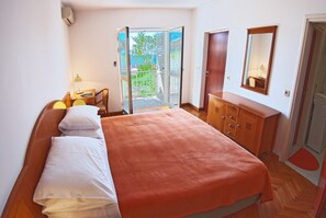 Ein Schlafzimmer mit einem Bett, einem Schreibtisch, einem Stuhl, einem Kleiderschrank und einer Glastür, die zu einem Außenbereich führt.