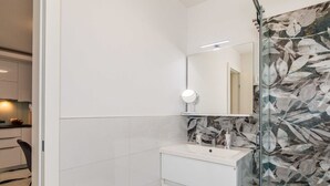 Casa de banho com toucador branco, espelho e cabine de duche em vidro.