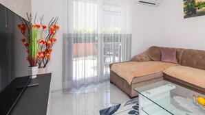 Uma sala de estar com um sofá, uma mesa de centro de vidro, uma televisão e uma planta decorativa.
