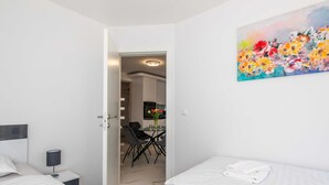 Quarto de hotel moderno com duas camas, área de refeições com mesa e cadeiras, e um quadro na parede.