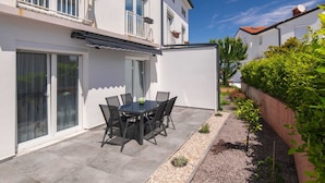 Uma casa moderna com um pátio, uma mesa de jantar com cadeiras e um pequeno jardim.