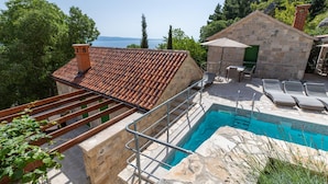 A pool area with a stone wall, a wooden deck, and a view of the sea. - Amazing Villa in Omis With Private Pool (Omis)