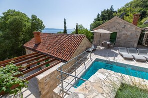 Ein Poolbereich mit Steinmauer, Holzterrasse und Blick auf das Meer.