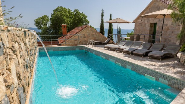 A swimming pool with a stone wall, lounge chairs, and a view of the sea. - Amazing Villa in Omis With Private Pool (Omis)