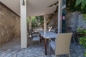 Eine Außenpatio-Terrasse mit Steinboden, einem langen Tisch, Korbstühlen und Blick auf eine steile Felswand.