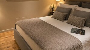 Een slaapkamer met een bed, kussens, een nachtkastje, een lamp, een schilderij en een raam.