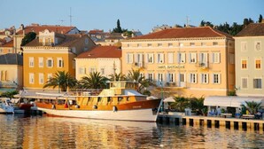 A waterfront hotel with a classic facade, a boat docked in front, and a clear view of the surrounding buildings. - Hotel APOKSIOMEN (Mali Lošinj)