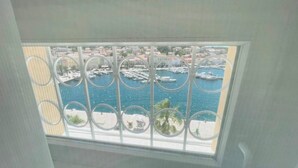 A view through a window with a metal railing, overlooking a marina with boats and buildings. - Hotel APOKSIOMEN (Mali Lošinj)