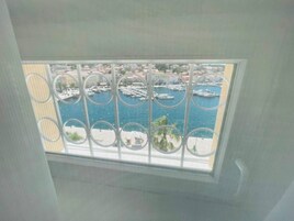 A view through a window with a metal railing, overlooking a marina with boats and buildings.