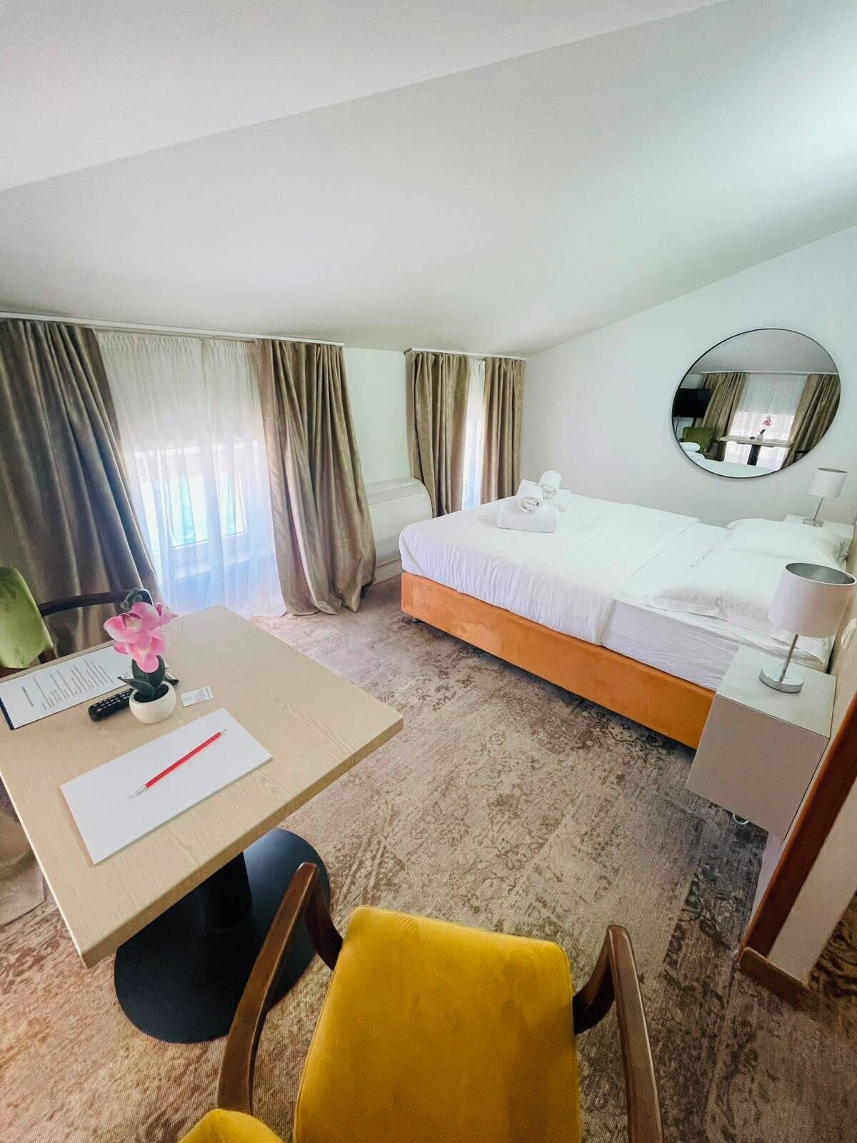 Une chambre d’hôtel avec un lit, un bureau, une chaise, un miroir et des rideaux.