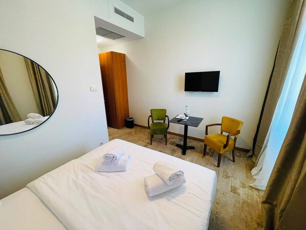 Habitación de hotel con cama, escritorio, dos sillas, televisor y espejo.
