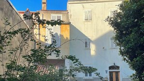 A building with a staircase leading to a wooden door, surrounded by greenery and a clear sky. - Hotel APOKSIOMEN (Mali Lošinj)