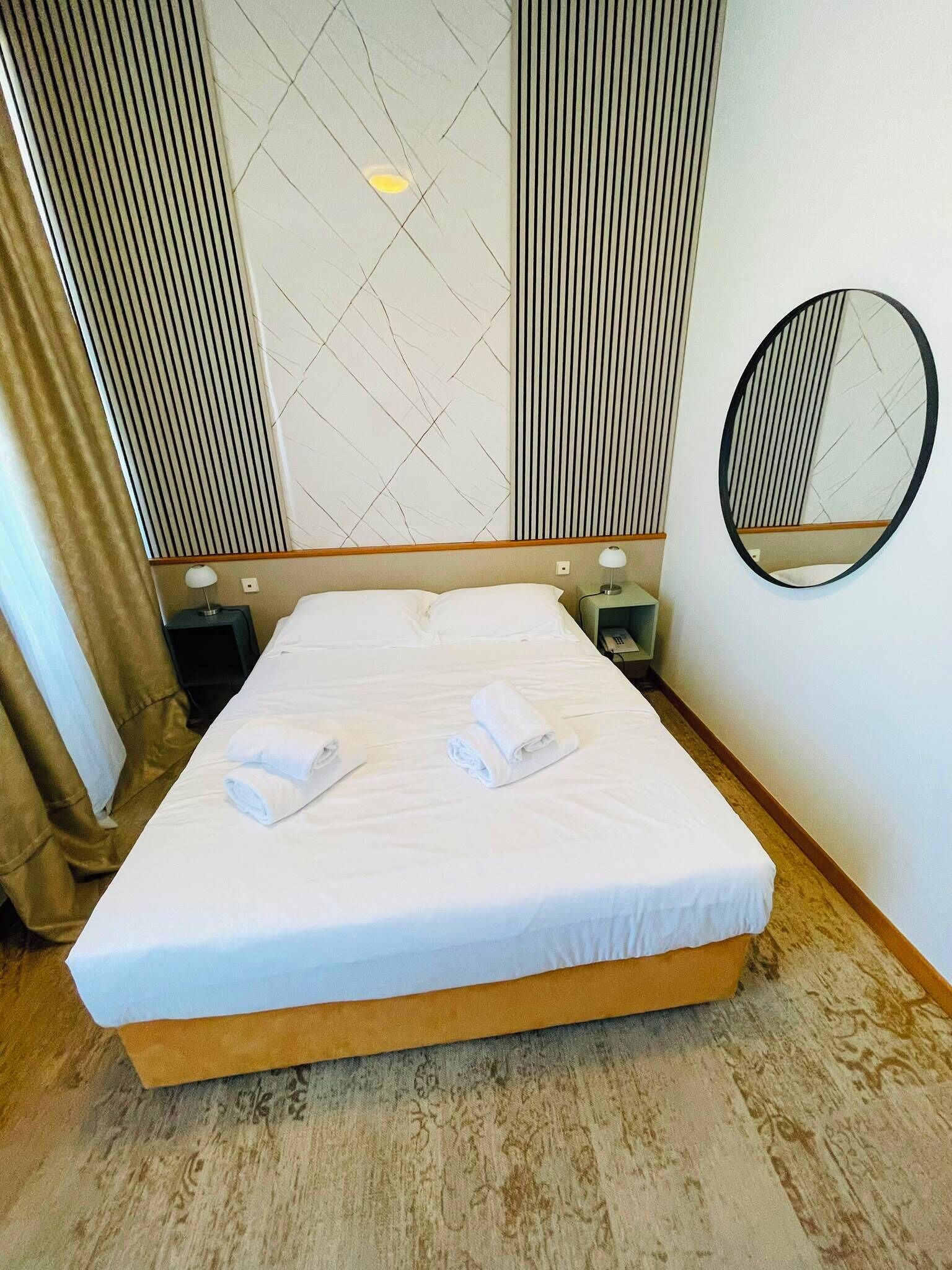 A hotel room with a bed, a bedside table, a lamp, a mirror, and a wall with a geometric pattern.