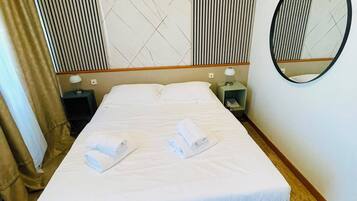 A hotel room with a bed, a bedside table, a lamp, a mirror, and a wall with a geometric pattern.