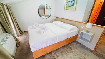 A hotel room with a bed, a bedside table with a lamp, a mirror, and a painting on the wall.