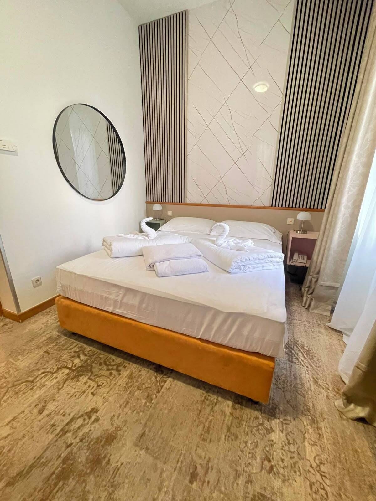 Una habitación de hotel con cama, espejo redondo, pared con diseño geométrico y mesita de noche con lámpara.