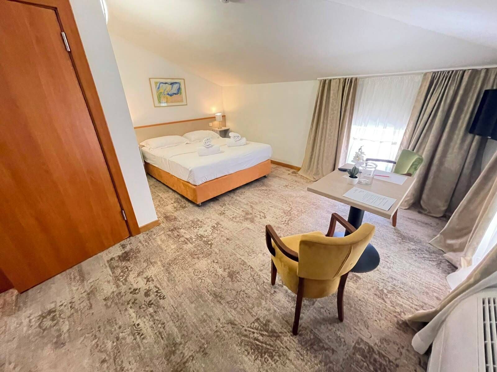 Ein Hotelzimmer mit einem Bett, einem Schreibtisch, einem Stuhl und einem fenster mit Vorhängen.