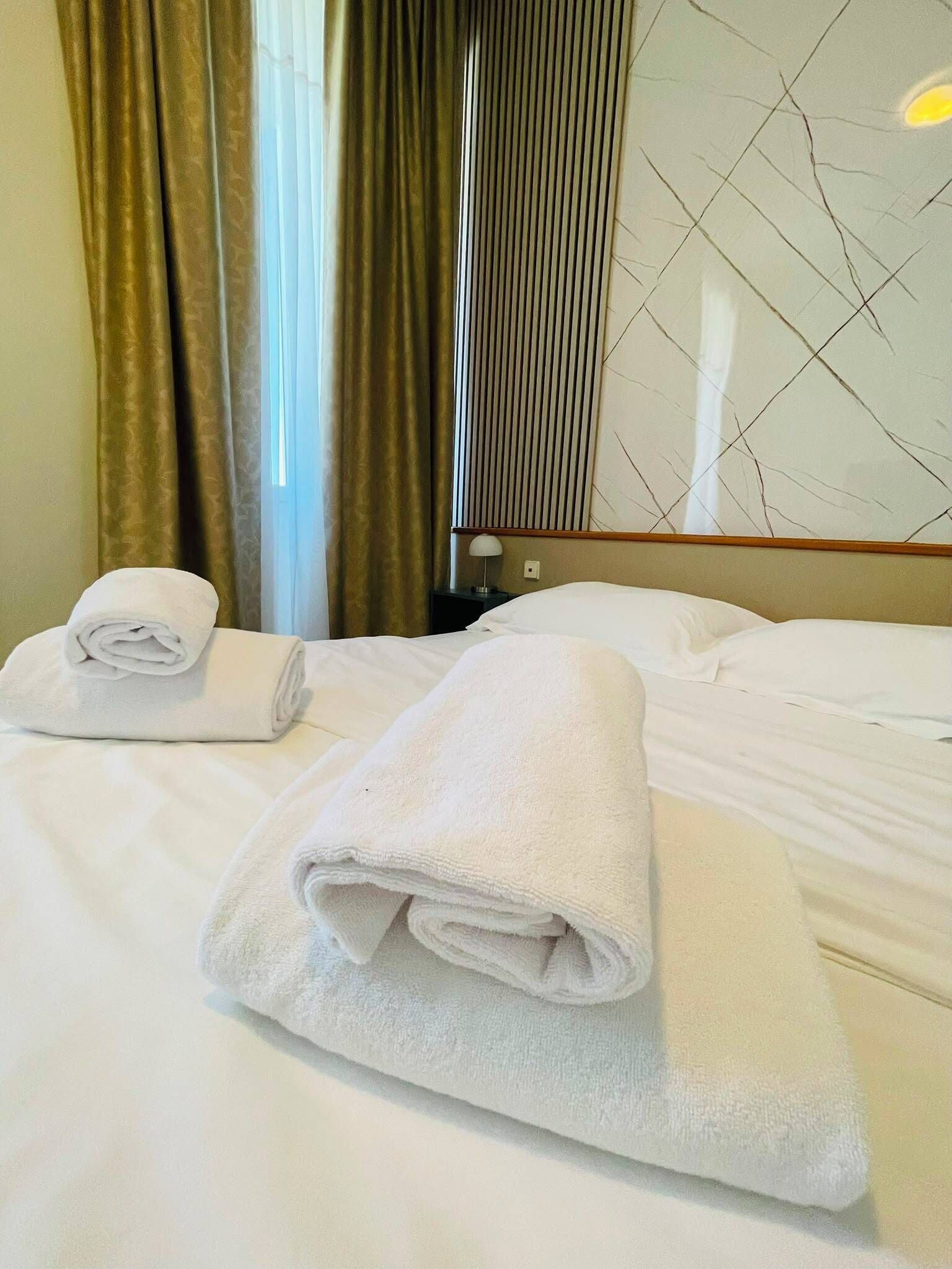 Quarto de hotel com duas camas bem arrumadas, uma janela com cortinas e uma parede com design geométrico.
