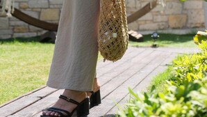 Una persona caminando sobre una cubierta de madera con una hamaca y un muro de piedra al fondo.