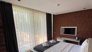 Un dormitorio moderno con una cama grande, un televisor montado en una pared de ladrillo y un balcón con cortinas.