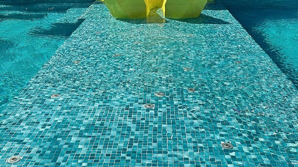 Un edificio moderno con amplios ventanales de vidrio y un área de piscina con una escultura geométrica amarilla.