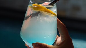 Una mano sosteniendo un vaso con una rodaja de limón y una pajita, cerca de una piscina.