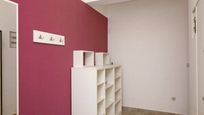 Una habitación con una pared rosa, una estantería blanca y suelo de baldosas.