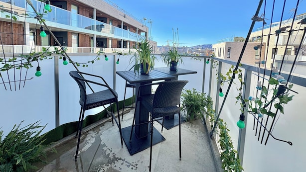 Un balcon avec une table et des chaises, des plantes en pot et des guirlandes lumineuses.