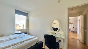 Une chambre à coucher avec un lit, un bureau doté d’un miroir et une vue sur la ville par la fenêtre.