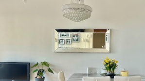 Un salon moderne doté d’un téléviseur à écran plat, d’une table à manger avec des chaises, d’une plante en pot, d’un aspirateur robot et d’un lustre.