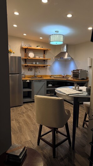 Una cocina moderna con horno empotrado, refrigerador de acero inoxidable, repisas de madera y una lámpara colgante.