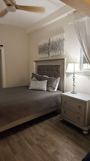 A bedroom with a bed, a nightstand, a lamp, and two wall-mounted paintings. - Charming Private Cottage with Resort-Style Pool Near Tampa Attractions (Tampa)