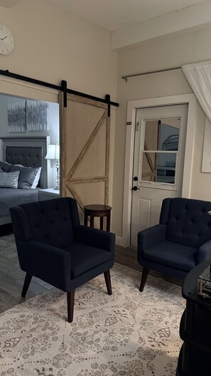 A room with a bed, two armchairs, a small table, a door with a window, and a clock on the wall. - Charming Private Cottage with Resort-Style Pool Near Tampa Attractions (Tampa)