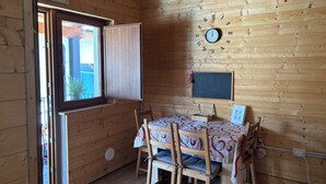 A wooden interior with a dining table, chairs, a clock, and a window.