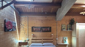 A wooden cabin bedroom with a bed, a wall-mounted clock, and a window with a view.