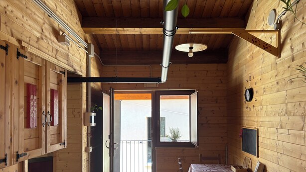 A wooden interior with a kitchen area, dining table, and a view through an open door.
