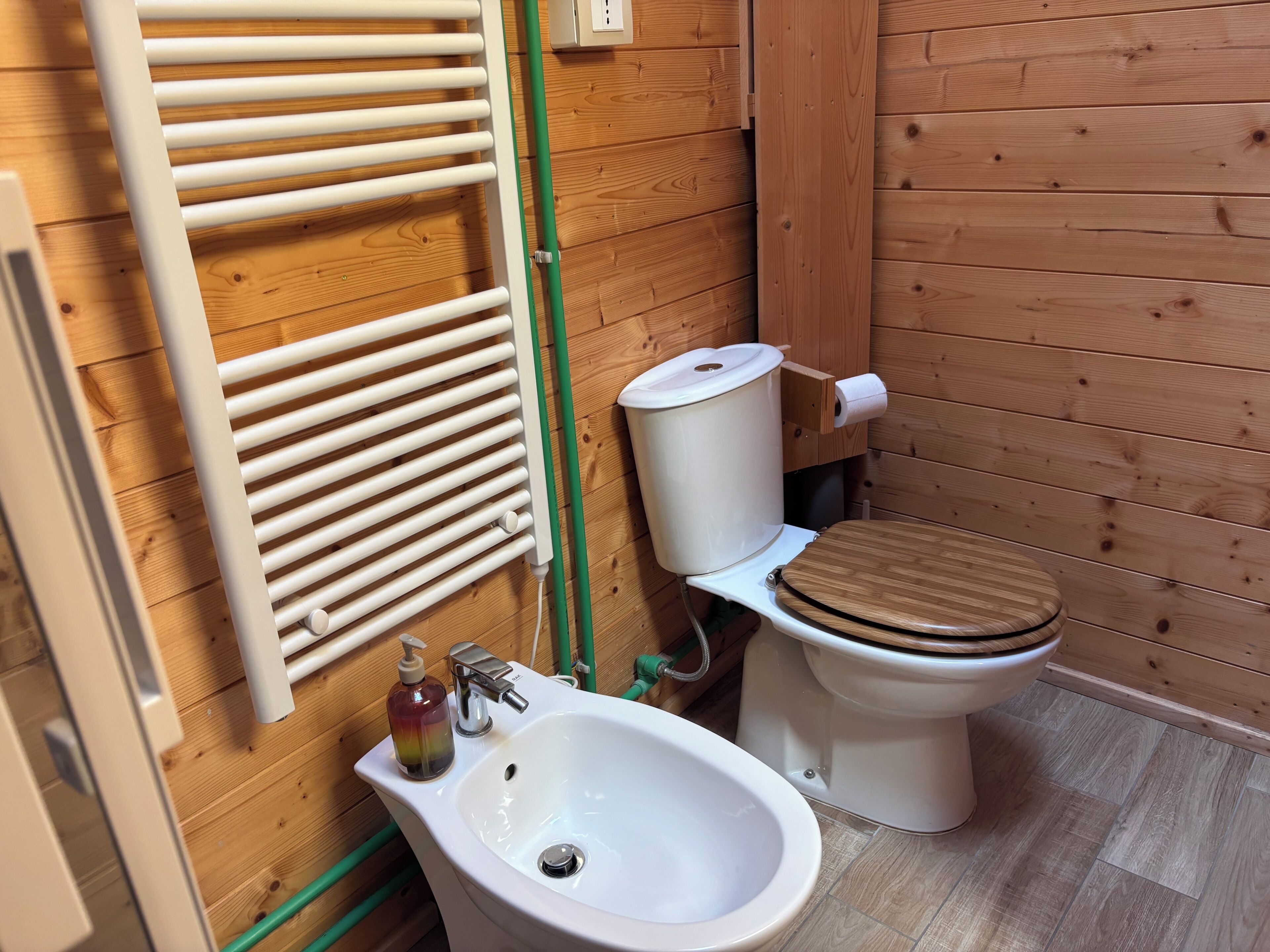 Une salle de bain aux murs lambrissés, équipée de toilettes, d’un bidet et d’un lavabo.