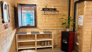 A wooden cabin interior with a window, a shelf with jars, a fireplace, and a bed.