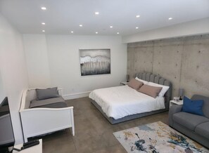 Ein modernes Schlafzimmer mit Bett, einer Couch, einem Schreibtisch und einem Gemälde an der Wand.