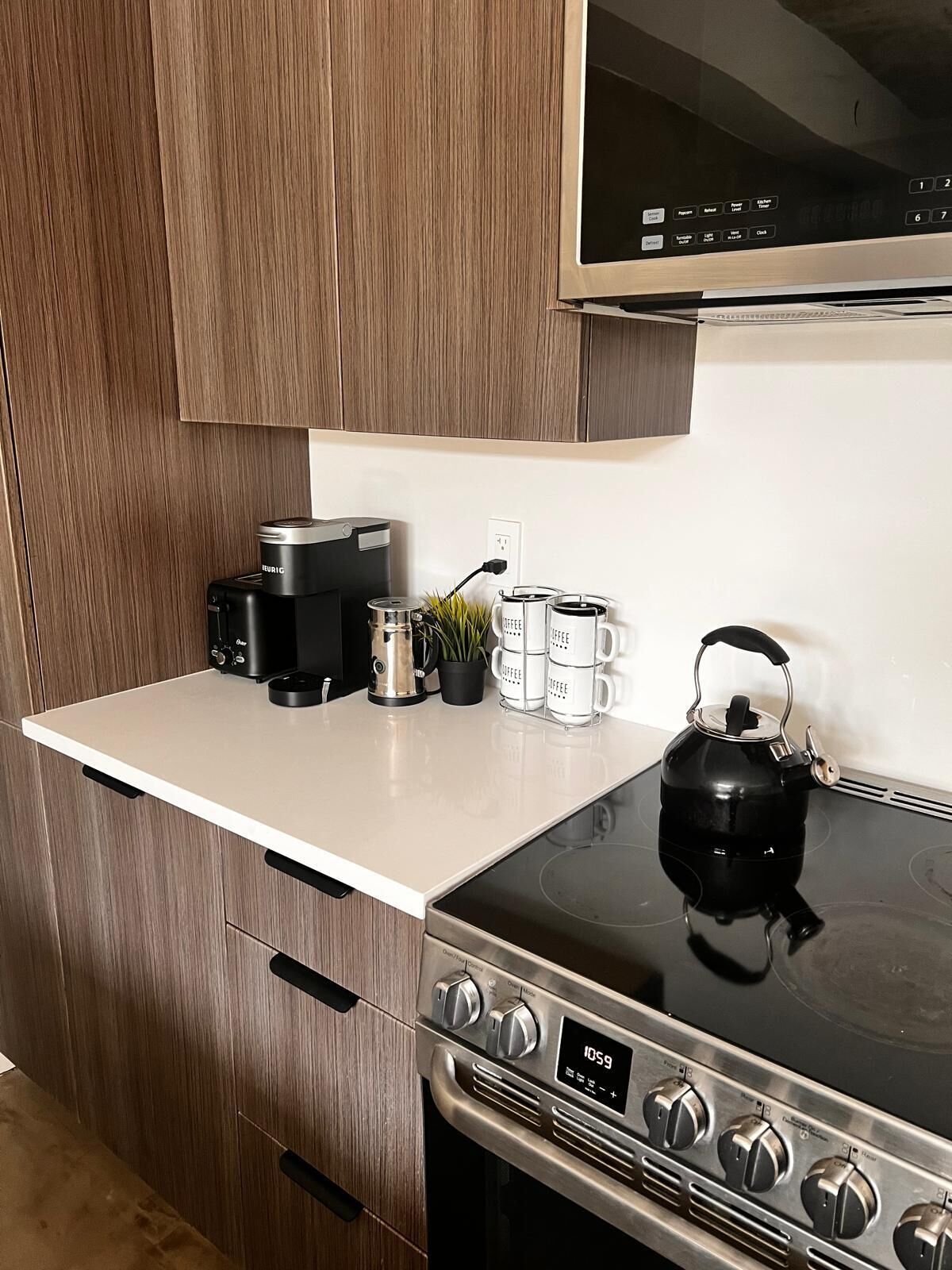 Une cuisine équipée d’une cuisinière, d’une machine à café, d’une bouilloire et de tasses à café posées sur le comptoir.