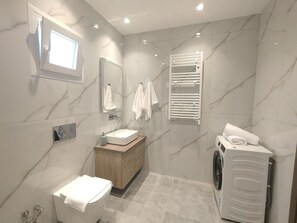 Et moderne badeværelse med vaskebord, håndvask, spejl, håndklædestang, toilet og en vaskemaskine.