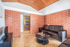 A room with a brick wall, a brown leather sofa, a round coffee table with fruit, and a wooden ceiling. - Villa Oura - Four Bedroom Villa, Sleeps 8 (Albufeira)
