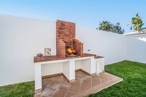 Un barbecue extérieur en briques, doté d’un plan de travail blanc, un panier de pommes de terre et un saladier rempli de légumes.