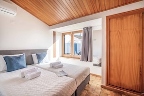 Une chambre avec deux lits, un plafond en bois, une fenêtre avec des rideaux et une armoire.